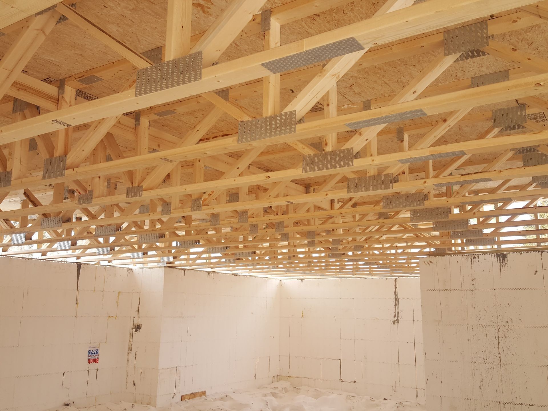 Interior view of a construction site with exposed wooden roof trusses and partially completed white concrete walls.