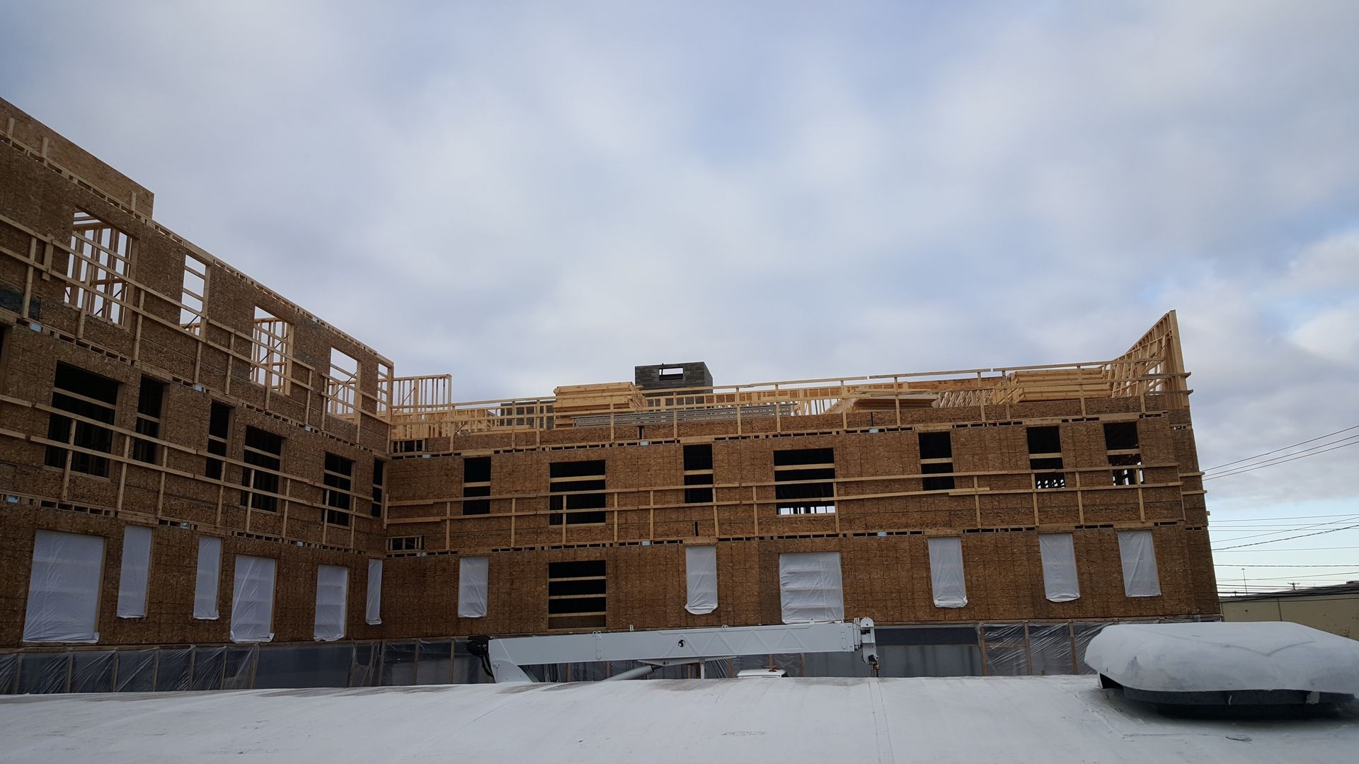 Partially constructed wooden building under a cloudy sky, showing framework and covered windows.