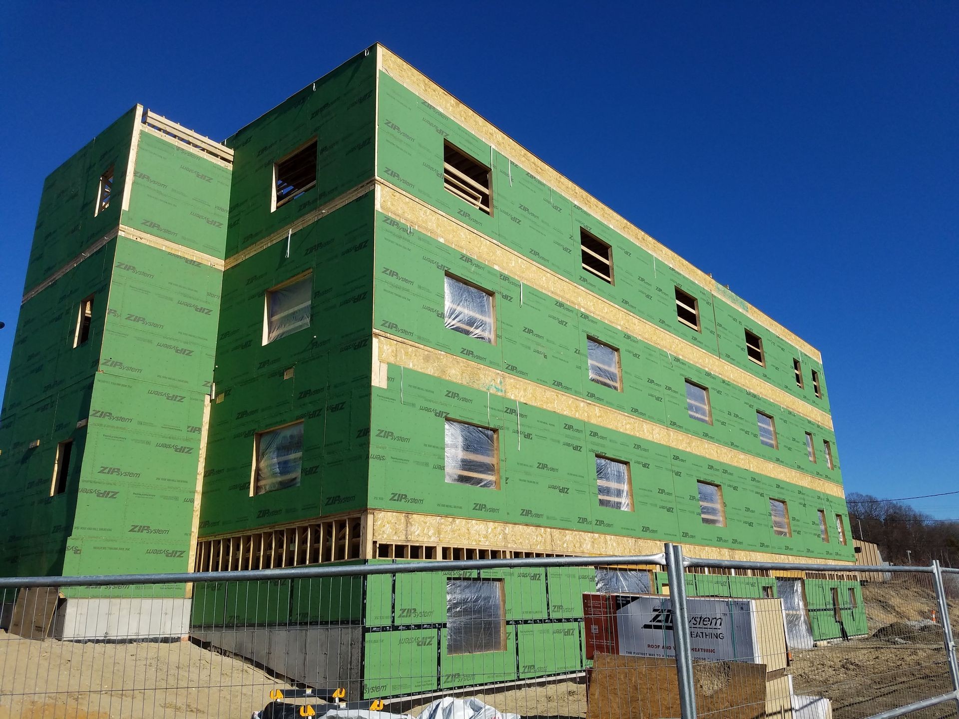 Partially constructed building with green sheathing and window openings on a clear day.