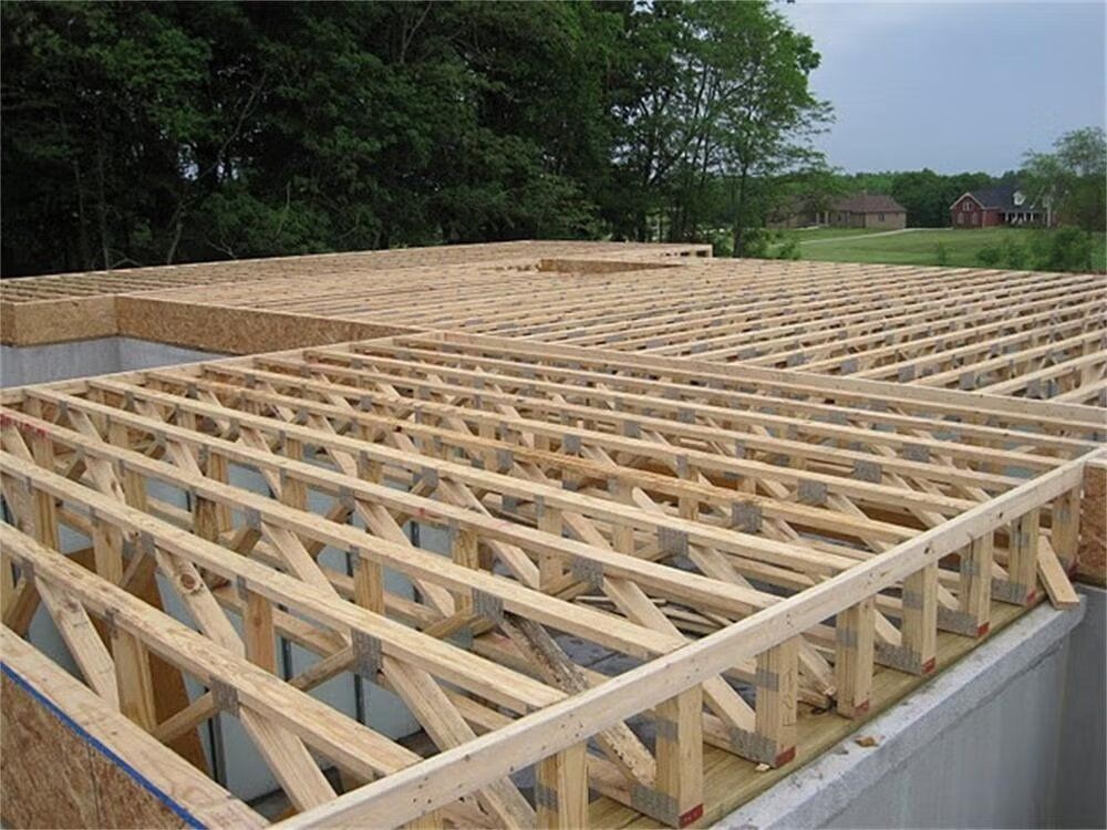 Wooden floor trusses on a construction site with trees and houses in the background.