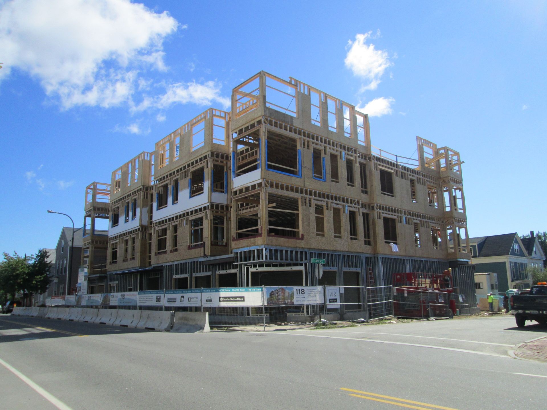 Multi-story building under construction with wooden framework, scaffolding, and a blue sky background.